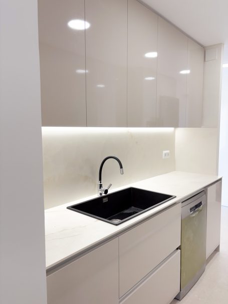 Cocina moderna con muebles claros, fregadero negro y luz suave en la pared.