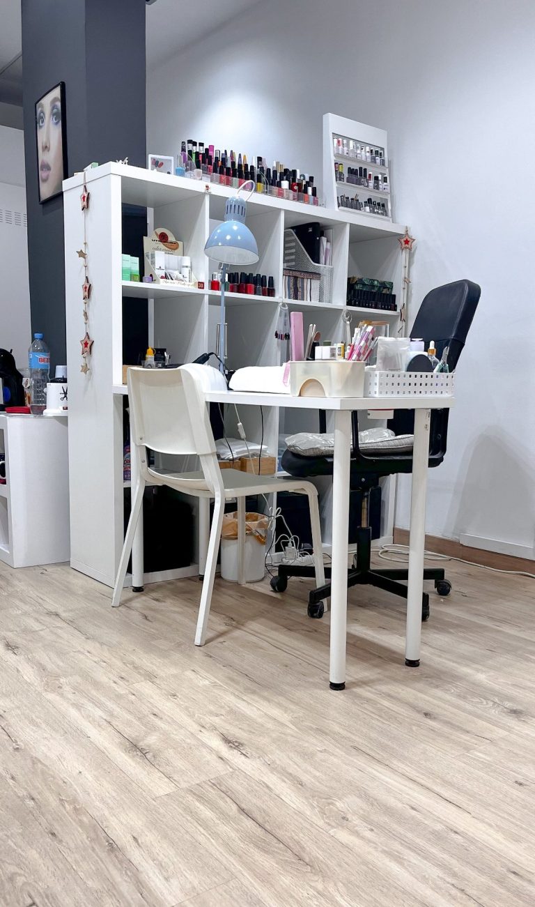 Mesa blanca con sillas en un espacio de oficina y estantería blanca al fondo.