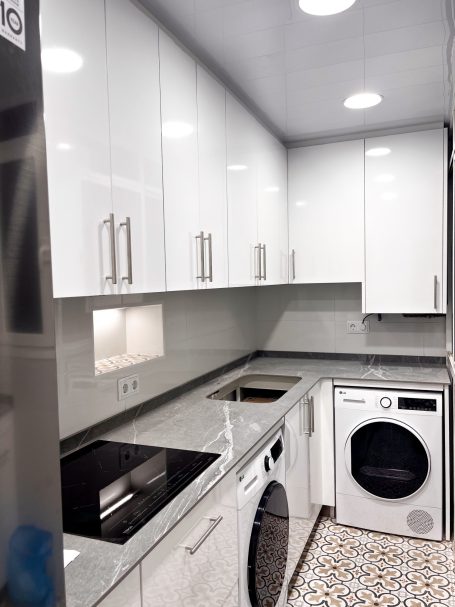 Cocina moderna con muebles blancos, encimera de mármol y electrodomésticos integrados.