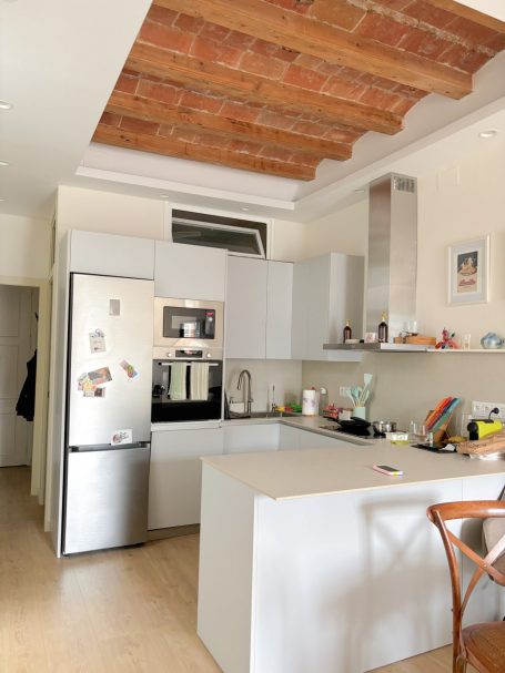 Cocina moderna con electrodomésticos de acero y una mesa de madera. Techo de ladrillo visto.