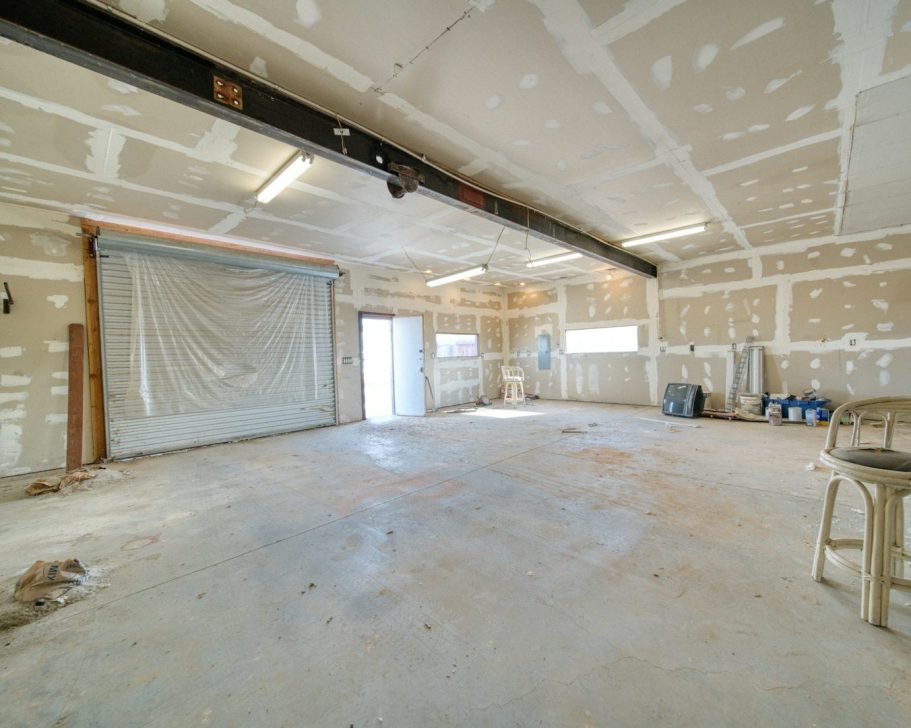 Sala amplia con paredes de pladur y suelo de cemento. Hay una puerta enrollable.