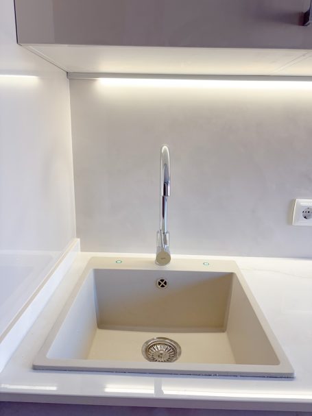 Fregadero blanco moderno con grifo y luz LED suave.