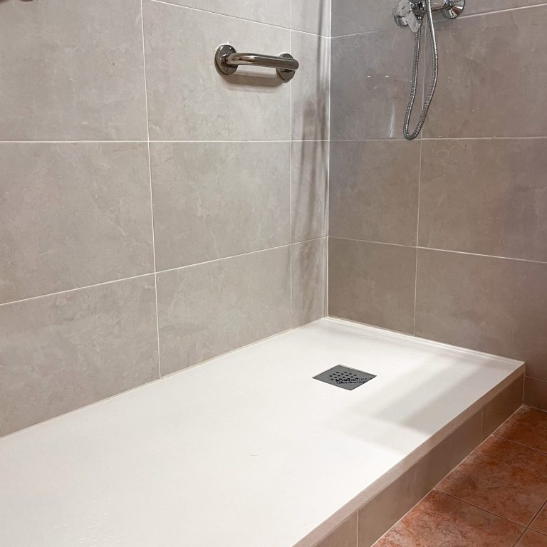 Ducha con paredes de azulejos grises y suelo de piedra, con grifo y barra de apoyo.