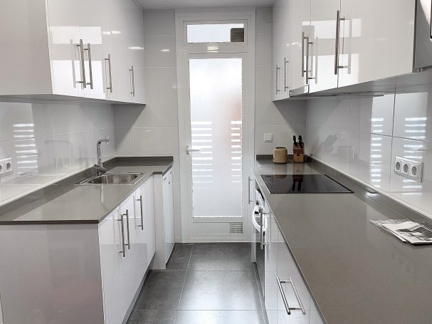 Cocina moderna y luminosa con muebles blancos y encimera de granito.