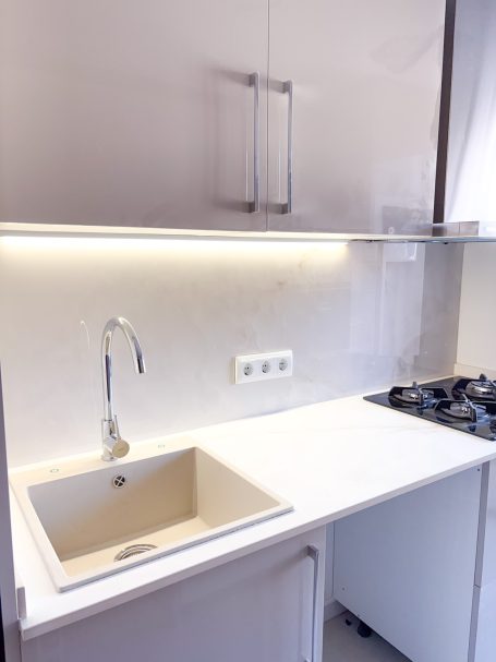 Cocina moderna con fregadero, encimera blanca y estufa al lado. Iluminación suave.