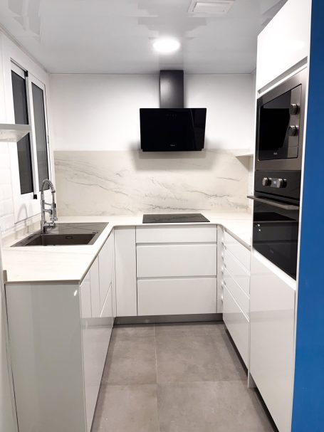 Cocina moderna con muebles blancos, encimeras claras y electrodomésticos integrados.