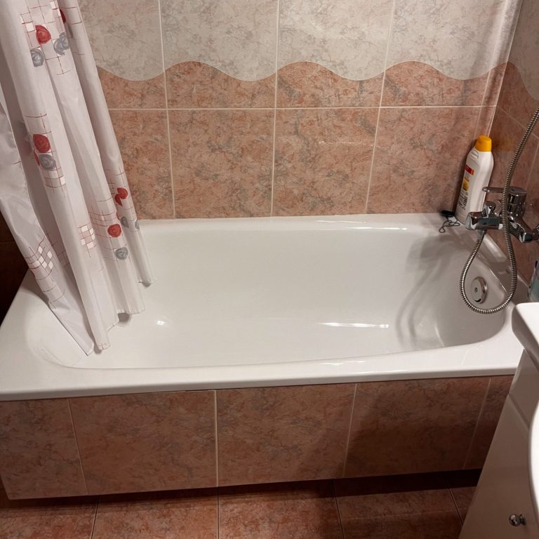 Baño con bañera blanca, cortina de ducha y productos de aseo en la esquina.