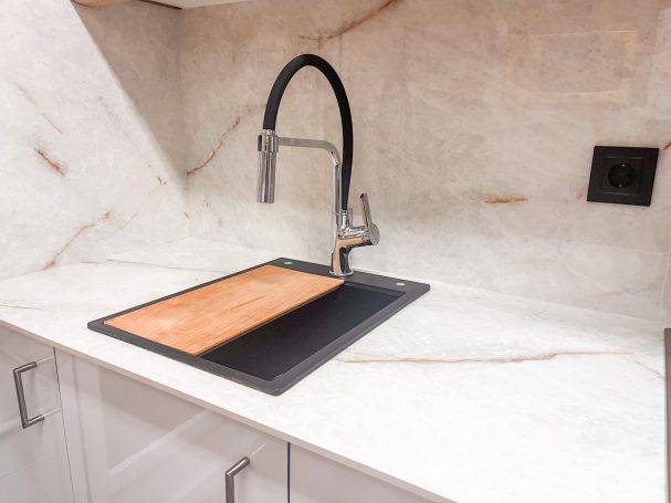 Grifo moderno sobre una encimera de mármol con una tabla de cortar de madera.