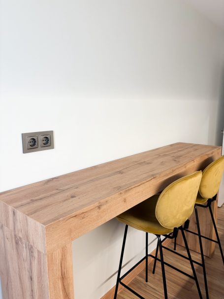 Barra de madera clara con dos taburetes amarillos en un ambiente minimalista.