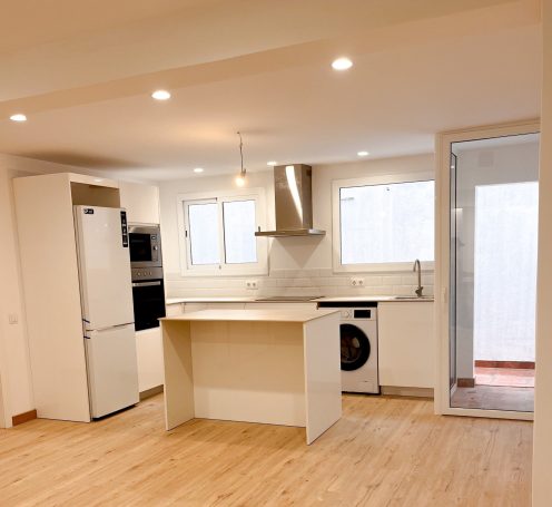 Cocina moderna y luminosa con electrodomésticos, isla central y acceso a un patio.