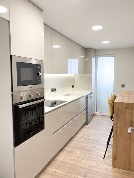 Cocina moderna con muebles claros, electrodomésticos de acero y una isla de madera.