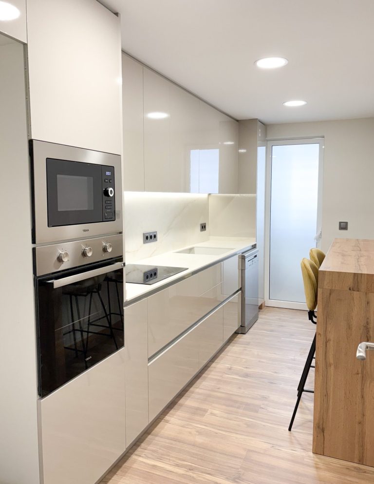 Cocina moderna con electrodomésticos integrados y barra de madera. Suelo de madera clara.