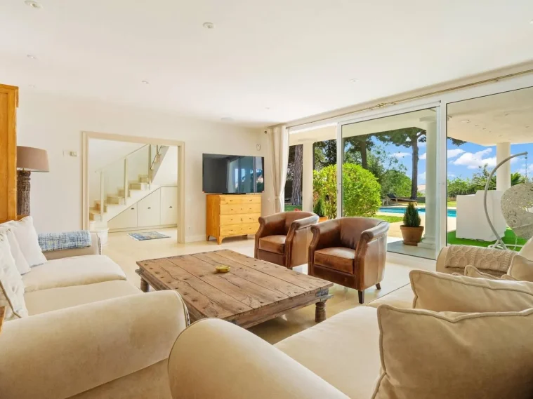 Sala de estar luminosa con sofá, sillas de cuero y vista al jardín y piscina.