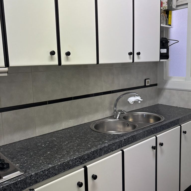 Cocina con muebles blancos, encimera negra y fregadero de dos senos.