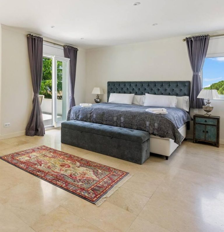 Habitación amplia y luminosa con cama grande, mesa de noche y alfombra roja.