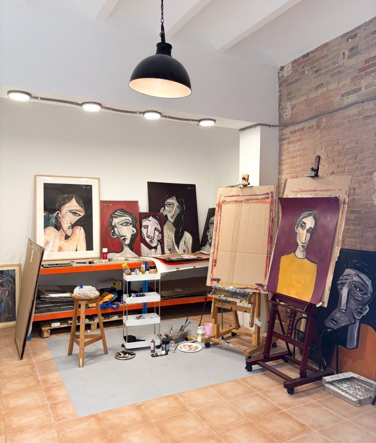 Estudio de arte con lienzos, caballetes y retratos en proceso de creación.