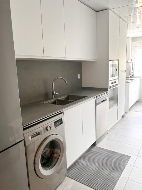 Cocina moderna con muebles blancos, fregadero y electrodomésticos integrados.