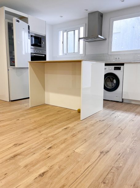 Cocina moderna con una isla, electrodomésticos y suelo de madera clara.